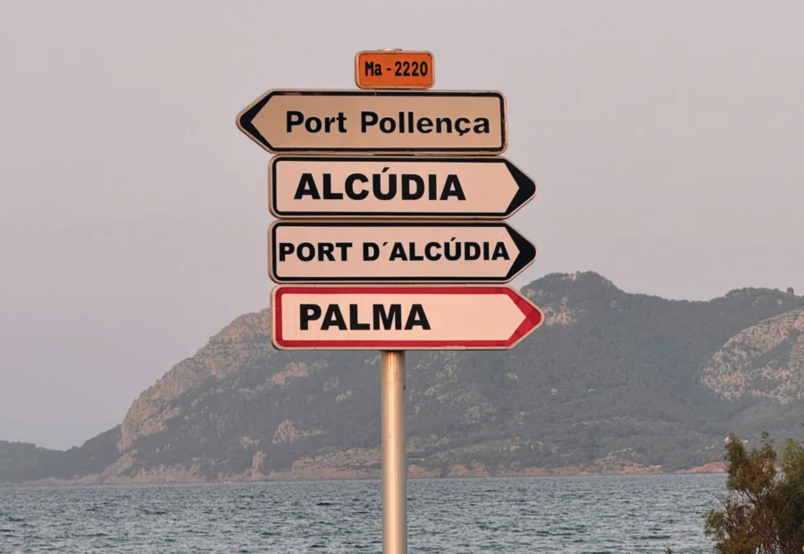 Señales hacia Port Pollença, Alcúdia y Palma con mar y montaña al fondo.