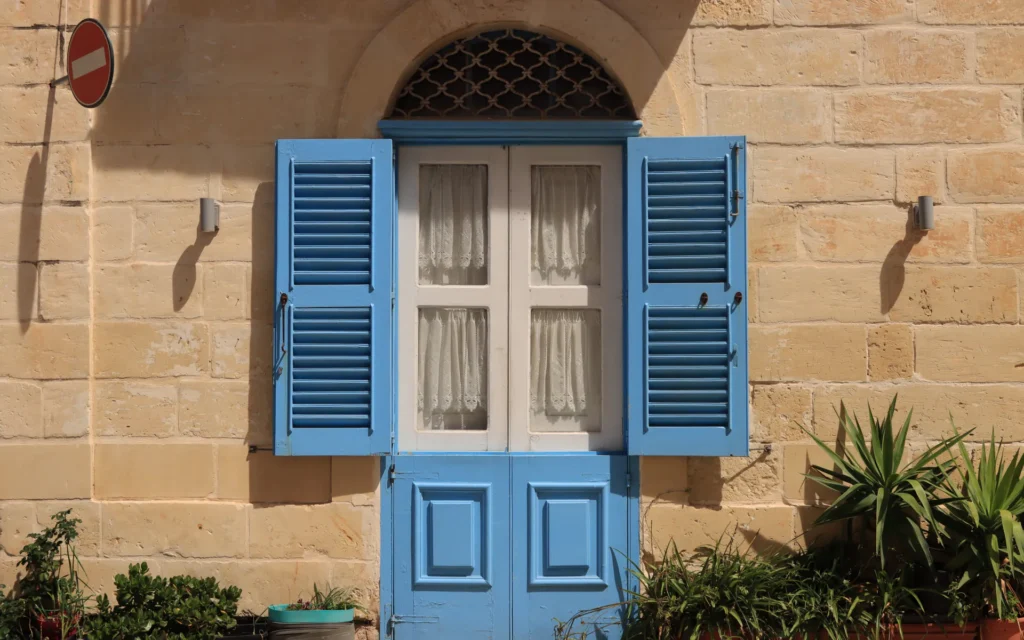 Puerta y contraventanas azules en una fachada de piedra con plantas.