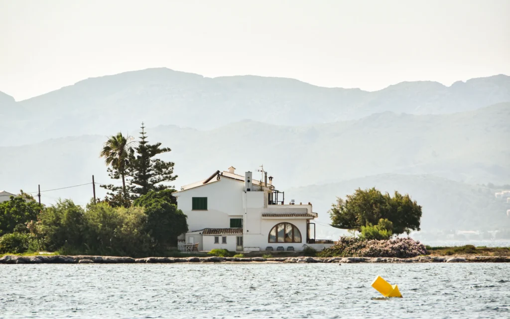 Casa blanca junto al mar con montañas al fondo.