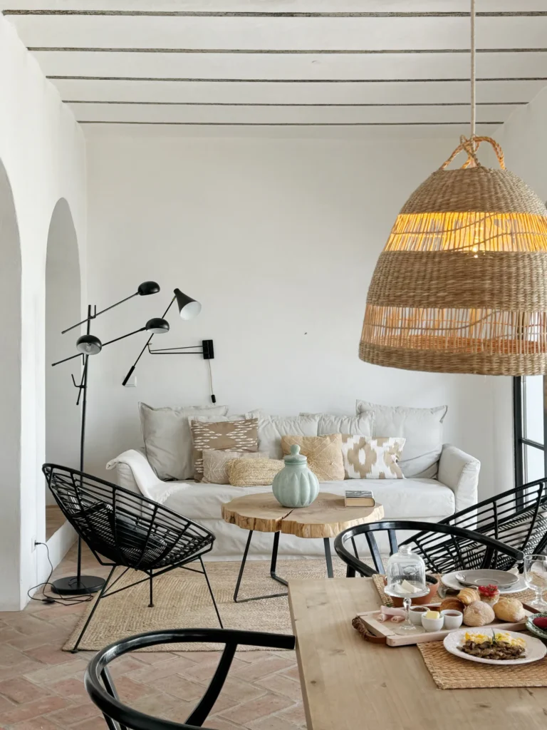 Salón luminoso con sofá blanco, sillas negras y mesa preparada.